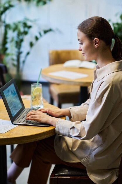 Jovem mulher de negócios em roupa de luxo tranquila sentada à mesa na frente do laptop