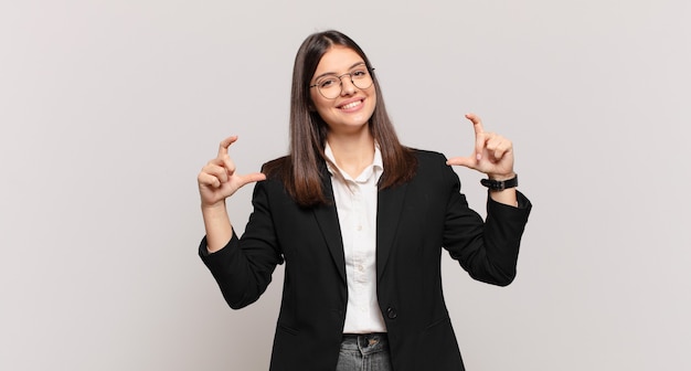 Jovem mulher de negócios emoldurando ou delineando seu próprio sorriso com as duas mãos, parecendo positiva e feliz, conceito de bem-estar