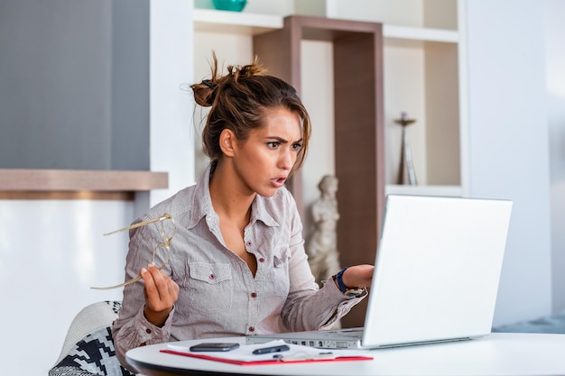 Jovem mulher de negócios entendendo mal seu laptop em sua mesa no escritório mulher trabalhando com laptop em casa ou escritório moderno expressão séria de confusão ou frustração