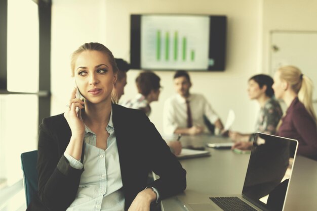 jovem mulher de negócios falando ao telefone no interior do escritório de inicialização moderna, equipe em grupo de reunião em segundo plano