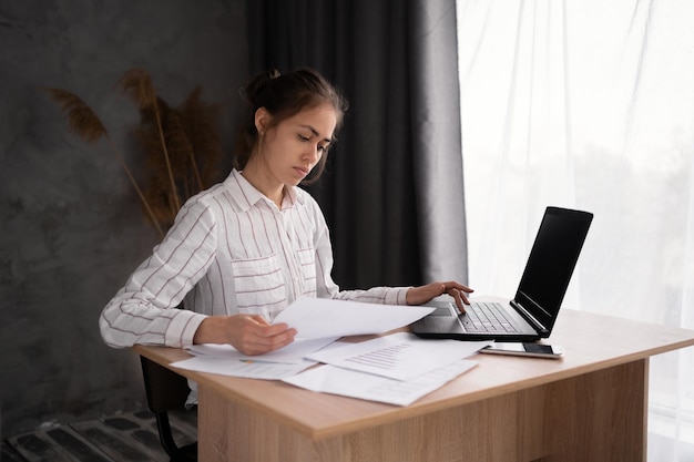 jovem mulher de negócios hispânica trabalhando com documentos usando laptop em escritório em casa analisando resultados de trabalho fazendo papelada no local de trabalho usando software de computador
