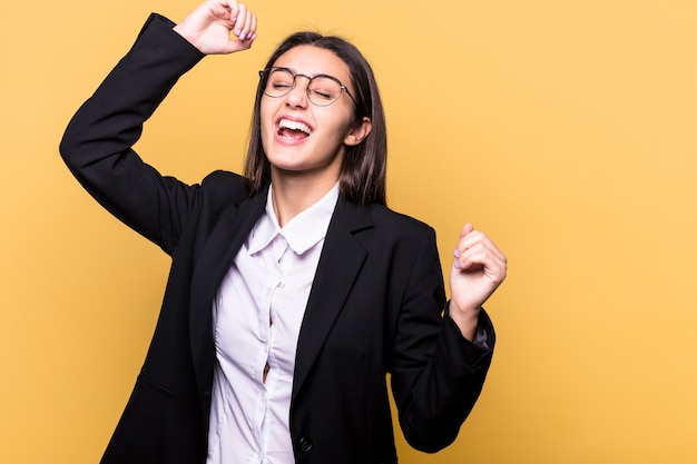 Jovem mulher de negócios indiana isolada na parede amarela comemorando um dia especial, pula e levanta os braços com energia