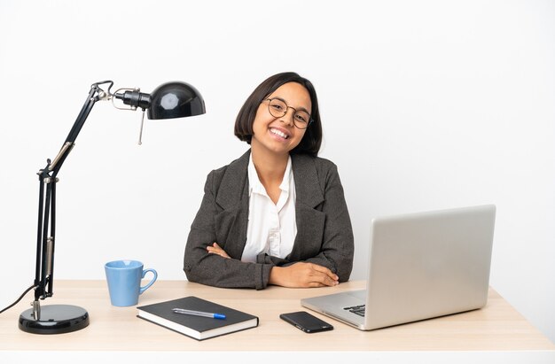 Jovem mulher de negócios misturados trabalhando em um escritório, posando com os braços na cintura e sorrindo