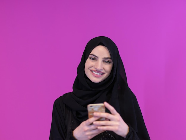 jovem mulher de negócios muçulmana moderna usando smartphone vestindo roupas hijab isoladas em fundo rosa