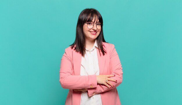 Jovem mulher de negócios parecendo uma empreendedora feliz, orgulhosa e satisfeita, sorrindo com os braços cruzados