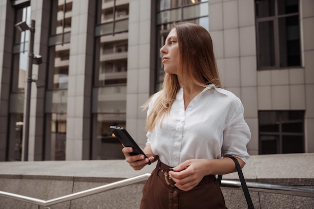 jovem mulher de negócios segurando o telefone do fundo do prédio de escritórios modernos