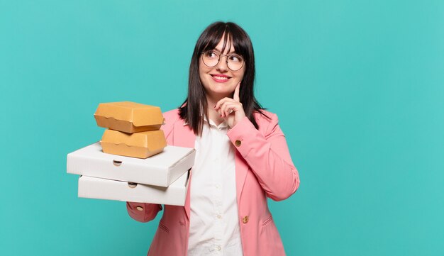 Jovem mulher de negócios sorrindo feliz e sonhando acordada ou duvidando, olhando para o lado