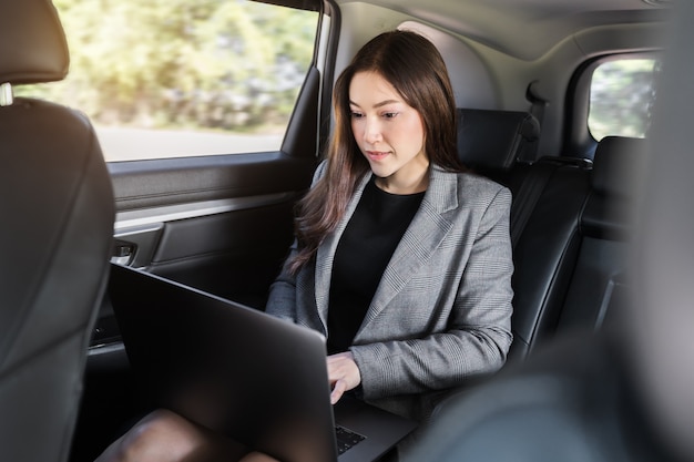 Jovem mulher de negócios usando um laptop enquanto está sentada no banco de trás do carro