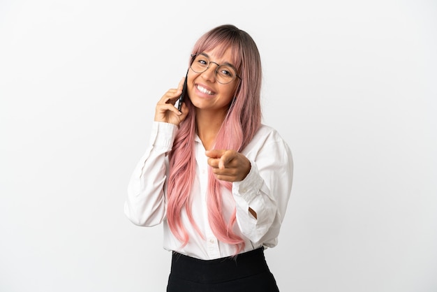 Jovem mulher de raça mista, negócios, com cabelo rosa segurando um celular isolado em um fundo rosa apontando para a frente com uma expressão feliz