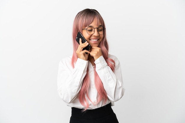 Jovem mulher de raça mista, negócios, com cabelo rosa segurando um celular isolado no fundo rosa, olhando para o lado e sorrindo