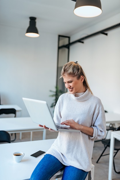 Jovem mulher de sorriso que guarda o laptop e que usa o no escritório moderno.