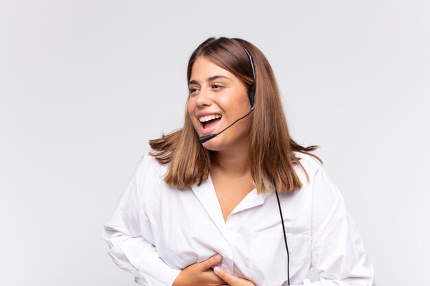 Jovem mulher de telemarketing rindo alto de uma piada hilária, sentindo-se feliz e alegre, se divertindo