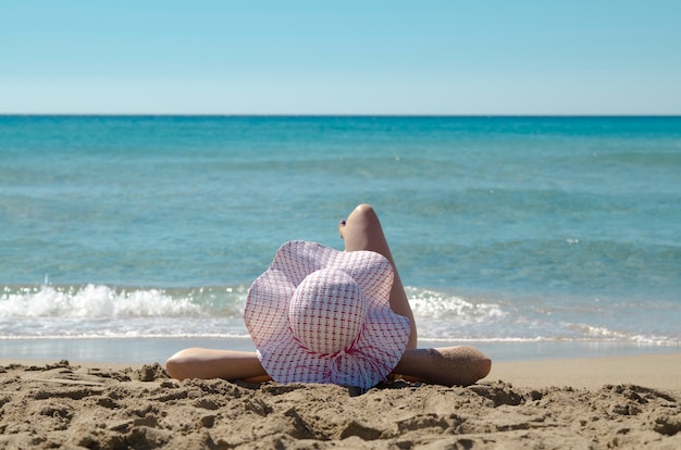 Jovem, mulher de volta na cabeça, chapéu de sol na praia de areia e relaxar de férias contra o mar.