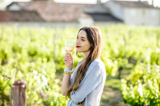 Jovem mulher degustando vinho em pé ao ar livre em um vinhedo na região de Bordeaux durante o pôr do sol na França