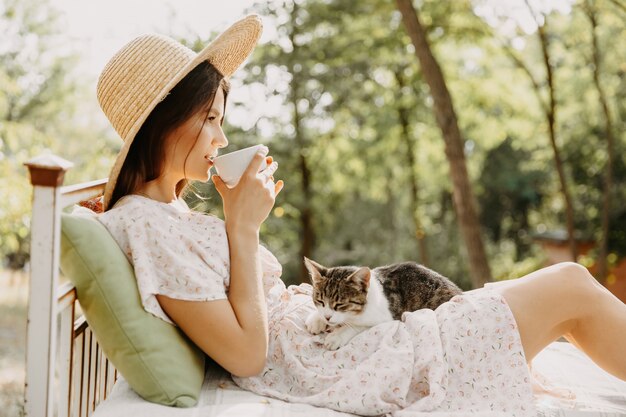 Jovem mulher deitada em uma cama, ao ar livre, no quintal e brincando com um gatinho