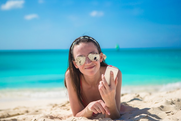 Jovem mulher deitada na areia branca e falando pelo telefone dela