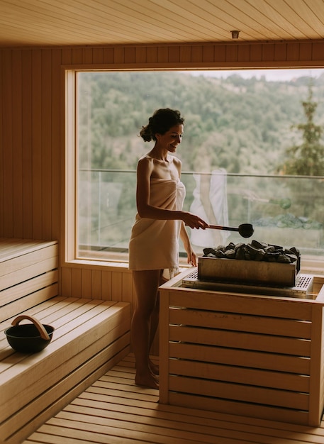 Jovem mulher derramando água em pedra quente na sauna