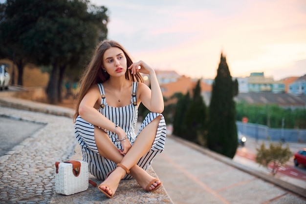 Jovem mulher descalça elegante posando na rua ao pôr do sol.