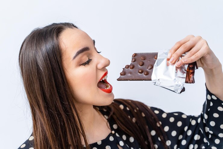 Foto jovem mulher desfruta de chocolate decadente dentro de casa uma jovem mulher está brincando se preparando para morder uma barra de chocolate enquanto sorri