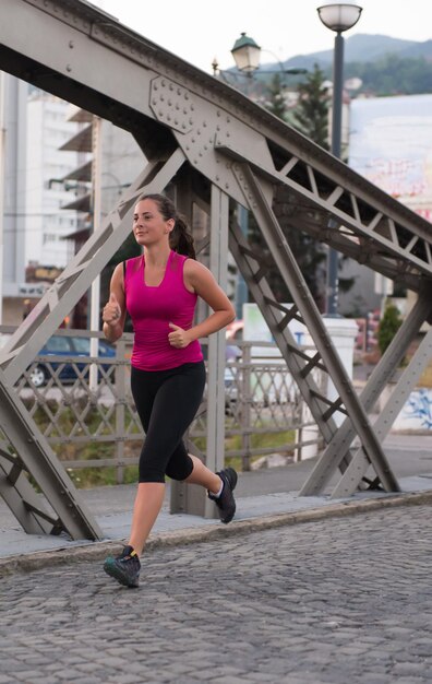 jovem mulher desportiva correndo pela ponte na manhã ensolarada na cidade