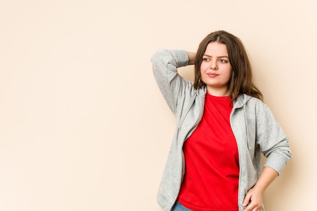 Jovem mulher desportiva curvilínea tocando na parte de trás da cabeça, pensando e fazendo uma escolha.