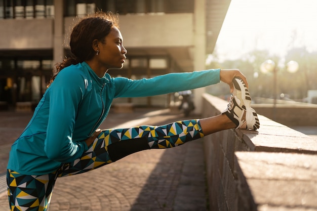 Jovem mulher desportiva fazendo alongamento ao ar livre em um dia ensolarado