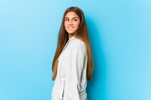 Jovem mulher desportiva parece de lado sorrindo, alegre e agradável.