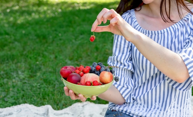 Jovem mulher detém uma tigela de frutas em um piquenique.