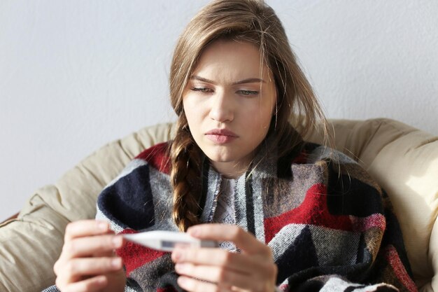 Foto jovem mulher doente com termômetro eletrônico em casa