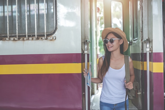 Jovem mulher dos viajantes com a trouxa que olha guarda um mapa na estação de trem. dia do turismo.