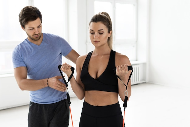 Jovem mulher durante o treino com um instrutor pessoal de fitness usando bandas de resistência de borracha no ginásio.