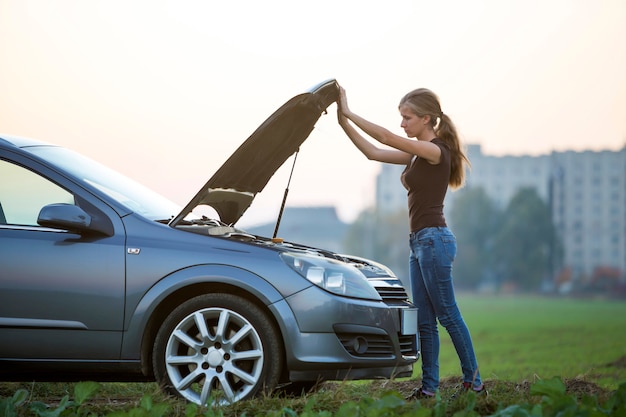Foto jovem mulher e um carro com capô estalado. transporte, problemas de veículos e conceito de avarias.