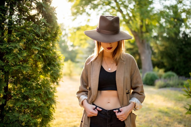 Jovem mulher elegante com chapéu e roupas em um jardim de aldeia na hora do sol