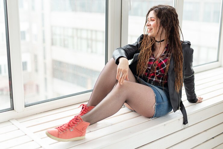 Foto jovem mulher elegante com dreadlocks, sentado no parapeito da janela.