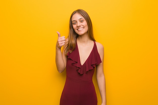 Jovem mulher elegante com um vestido, sorrindo e levantando o polegar