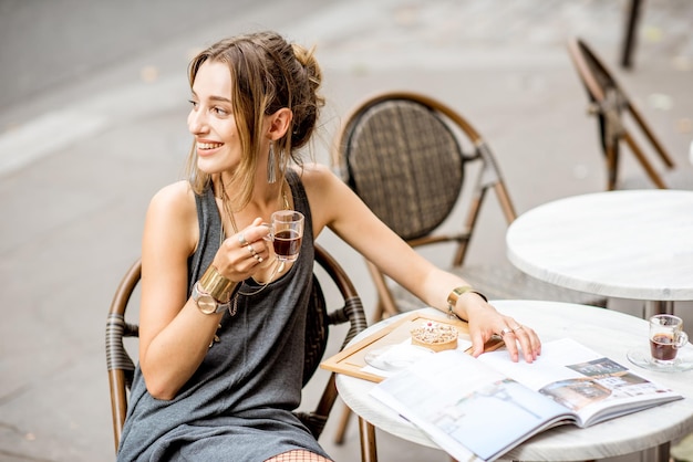 Jovem mulher elegante em um vestido cinza tomando café ao ar livre em um café em Paris