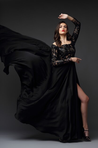 Jovem mulher elegante em um vestido preto longo. Elegant Flying Fabric, vestido de noite.