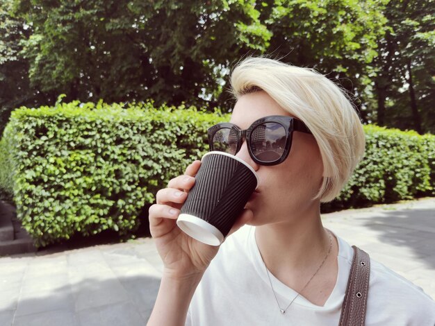 Jovem mulher elegante tomando café para ir a um parque.