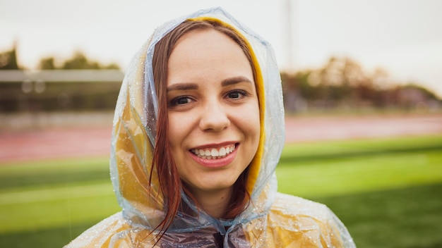 Jovem mulher em capa de chuva em tempo chuvoso Retrato de mulher positiva em casaco impermeável molhado