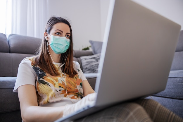 Jovem mulher em casa trabalhando no laptop, escritório remoto. Compras online durante quarentena e medidas preventivas de corona. Conversando com colegas, tendo reunião online. Ficar em casa.