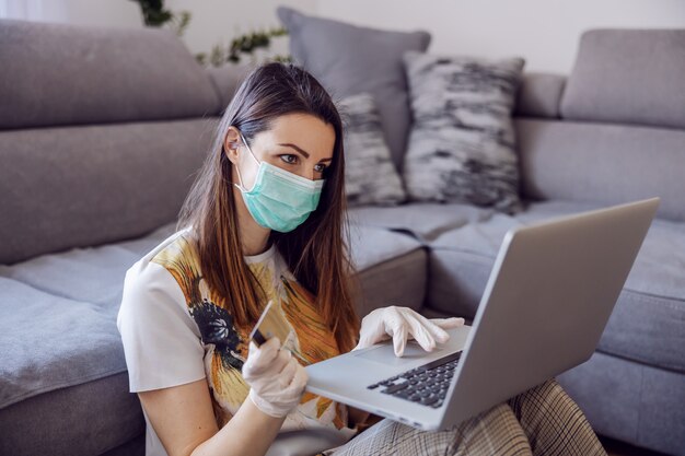 Jovem mulher em casa trabalhando no laptop, escritório remoto. Compras online durante quarentena e medidas preventivas de corona. Ficar em casa.