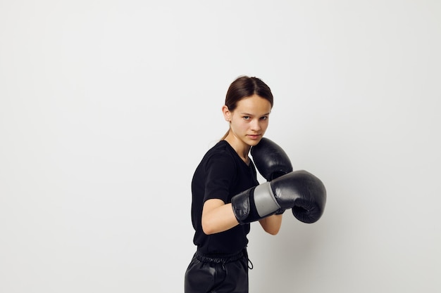 Jovem mulher em luvas de boxe de uniforme esportivo preto posando de fundo isolado