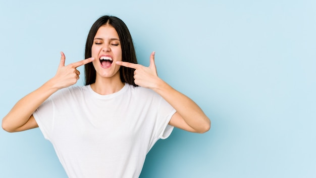 Jovem mulher em sorrisos azuis, apontando os dedos na boca.