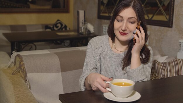 Jovem mulher em um café bebendo chá e falando ao telefone.