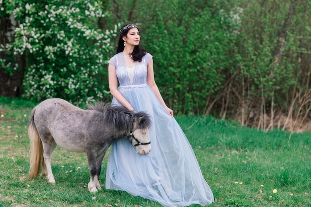 Jovem mulher em um lindo vestido na floresta com um pônei cinza