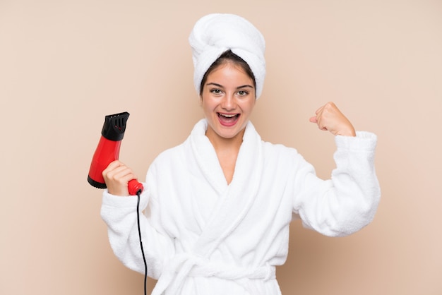 Jovem mulher em um roupão de banho com secador de cabelo comemorando uma vitória