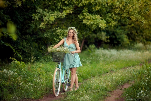 Jovem mulher em um vestido com uma bicicleta e um buquê de flores silvestres