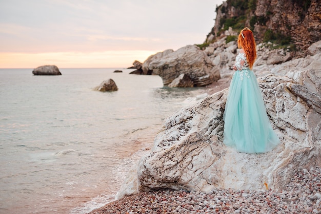 Jovem mulher em um vestido de luxo fica na costa do mar Adriático