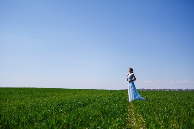 Jovem mulher em um vestido longo azul sobre um fundo de campo verde. Retrato da moda de uma linda garota com um sorriso no rosto