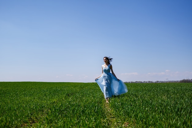 Jovem mulher em um vestido longo azul sobre um fundo de campo verde. retrato da moda de uma linda garota com um sorriso no rosto